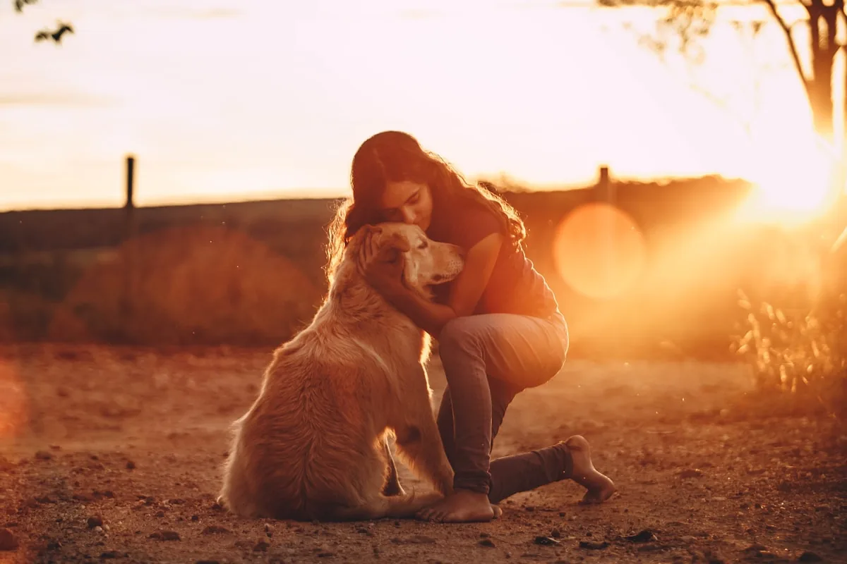 A woman embracing her dog outdoors at sunset